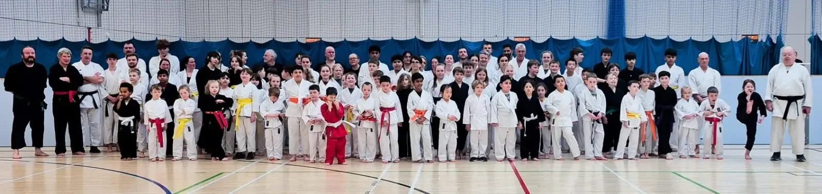 Members of the association lined up together in a sports hall, juniors at the front and seniors behind