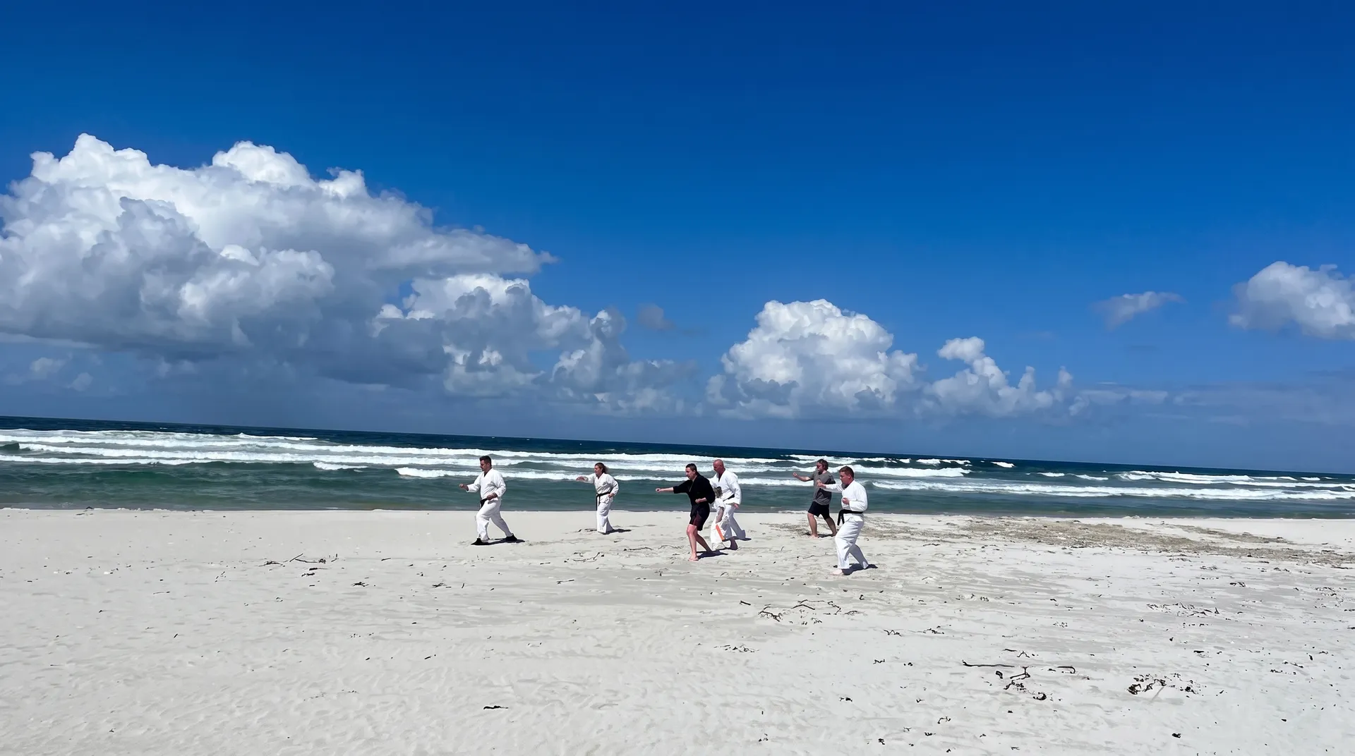 Members training on a white sand beach under a blue sky